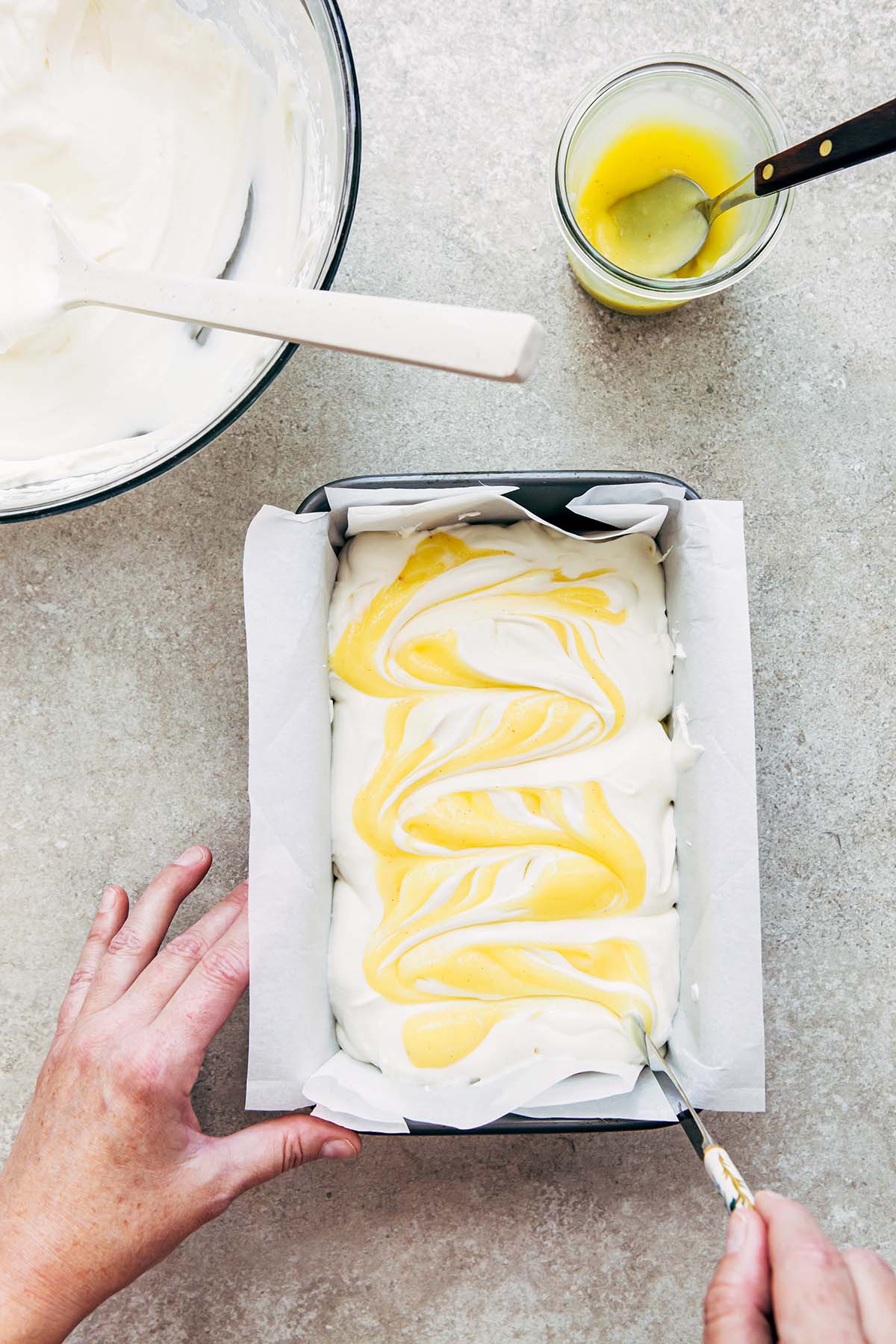 A hand swirling lemon curd through whipped cream with a butter knife.