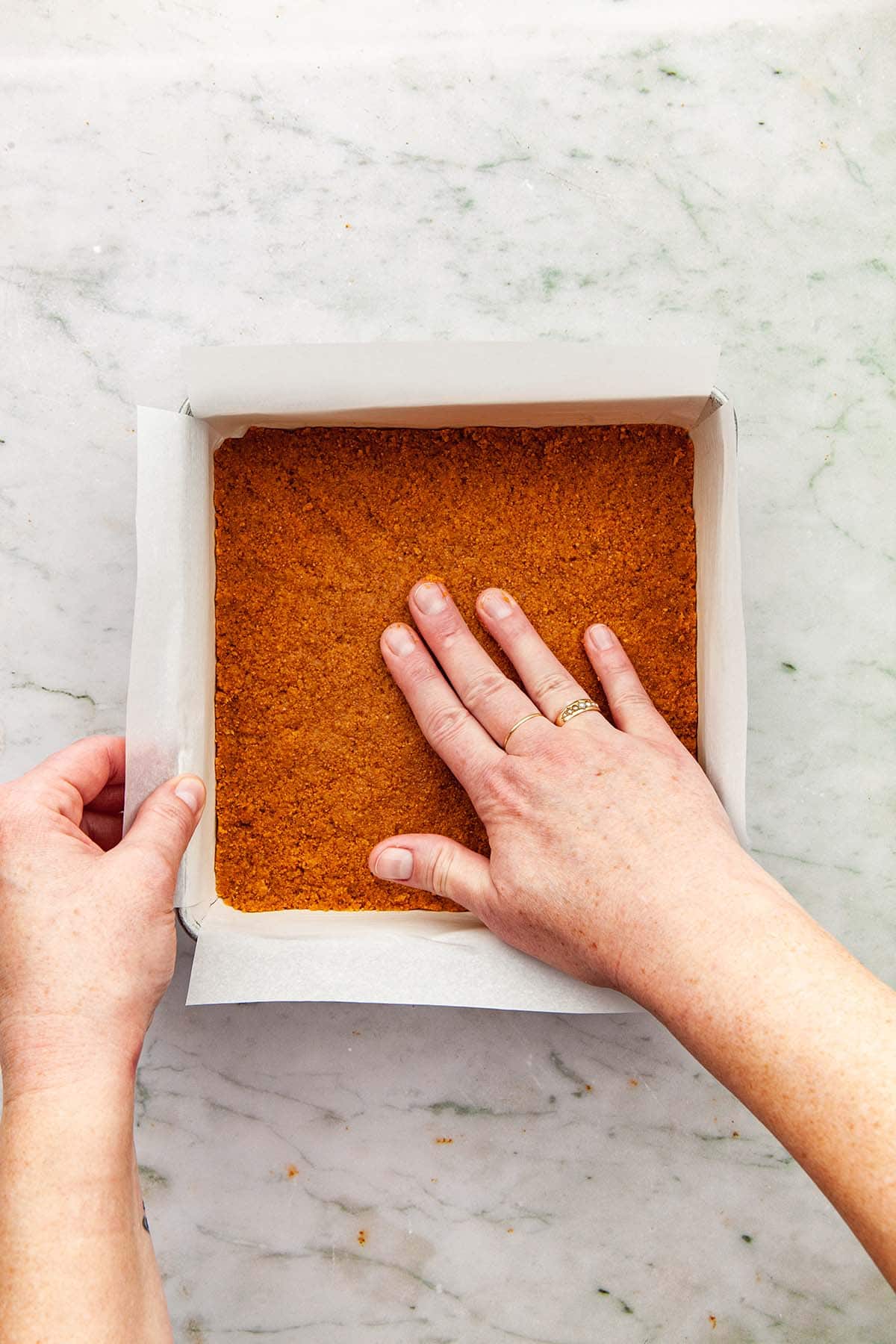 A hand finishing pressing graham crumbs into a square pan.
