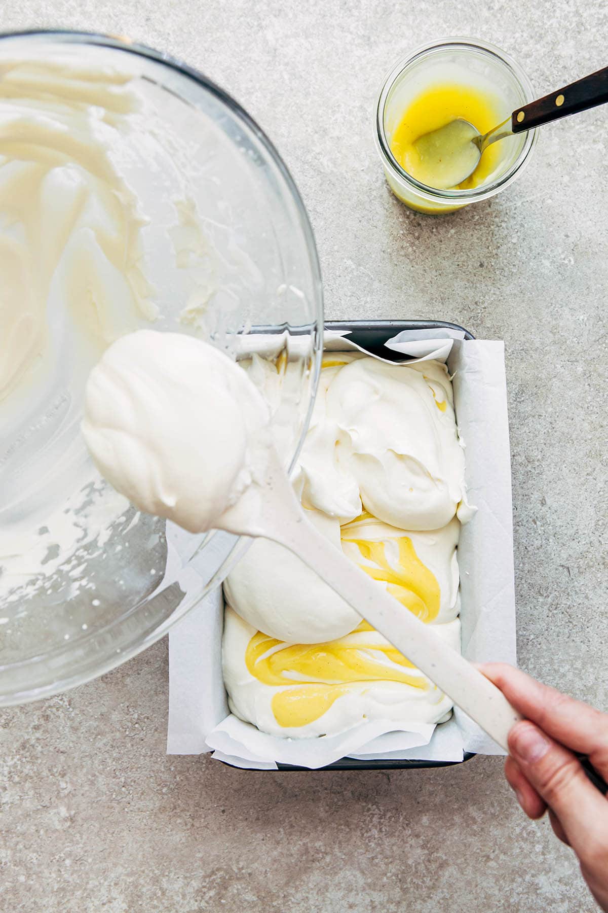 A hand spooning whipped cream into a tin of no-churn ice cream.