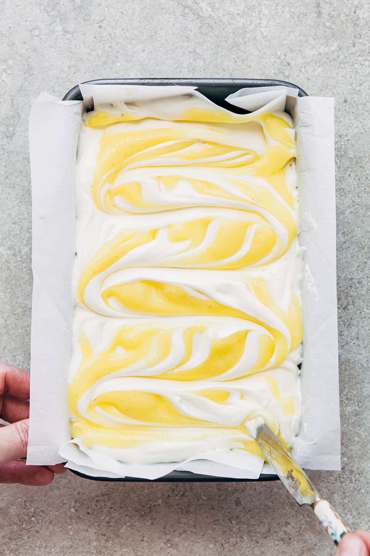 A hand swirling lemon curd through no churn ice cream with a butter knife.