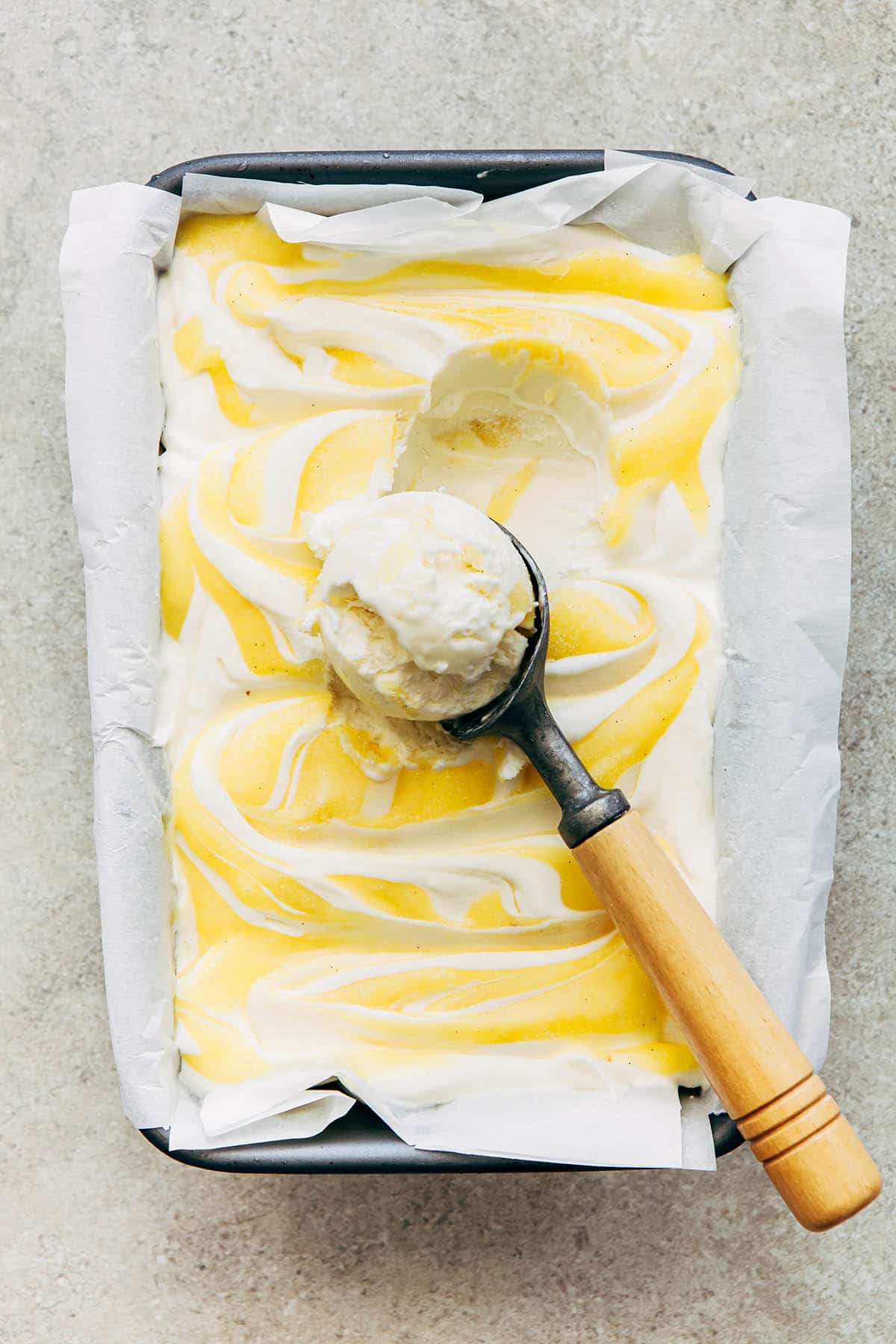 A loaf pan of lemon curd ice cream with a scoop on top.