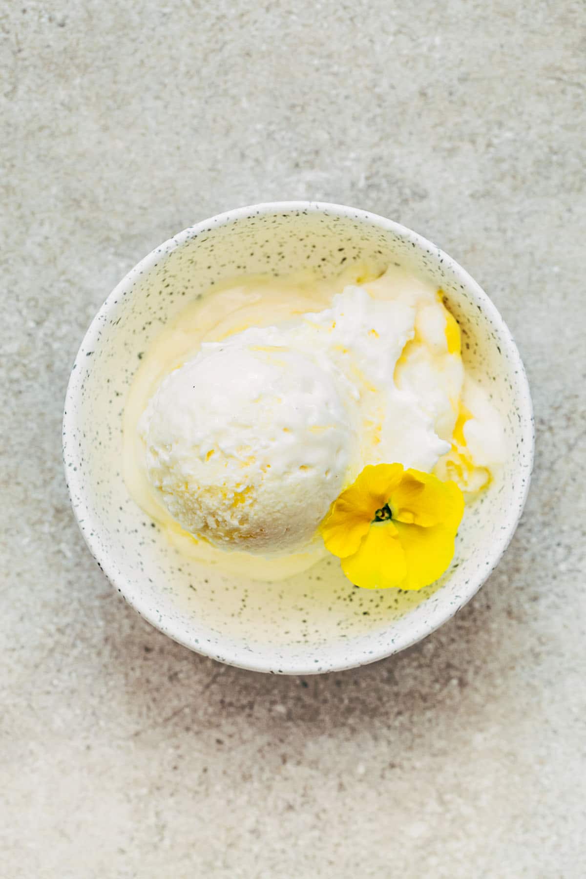 A small dish of ice cream garnished with a yellow pansy.