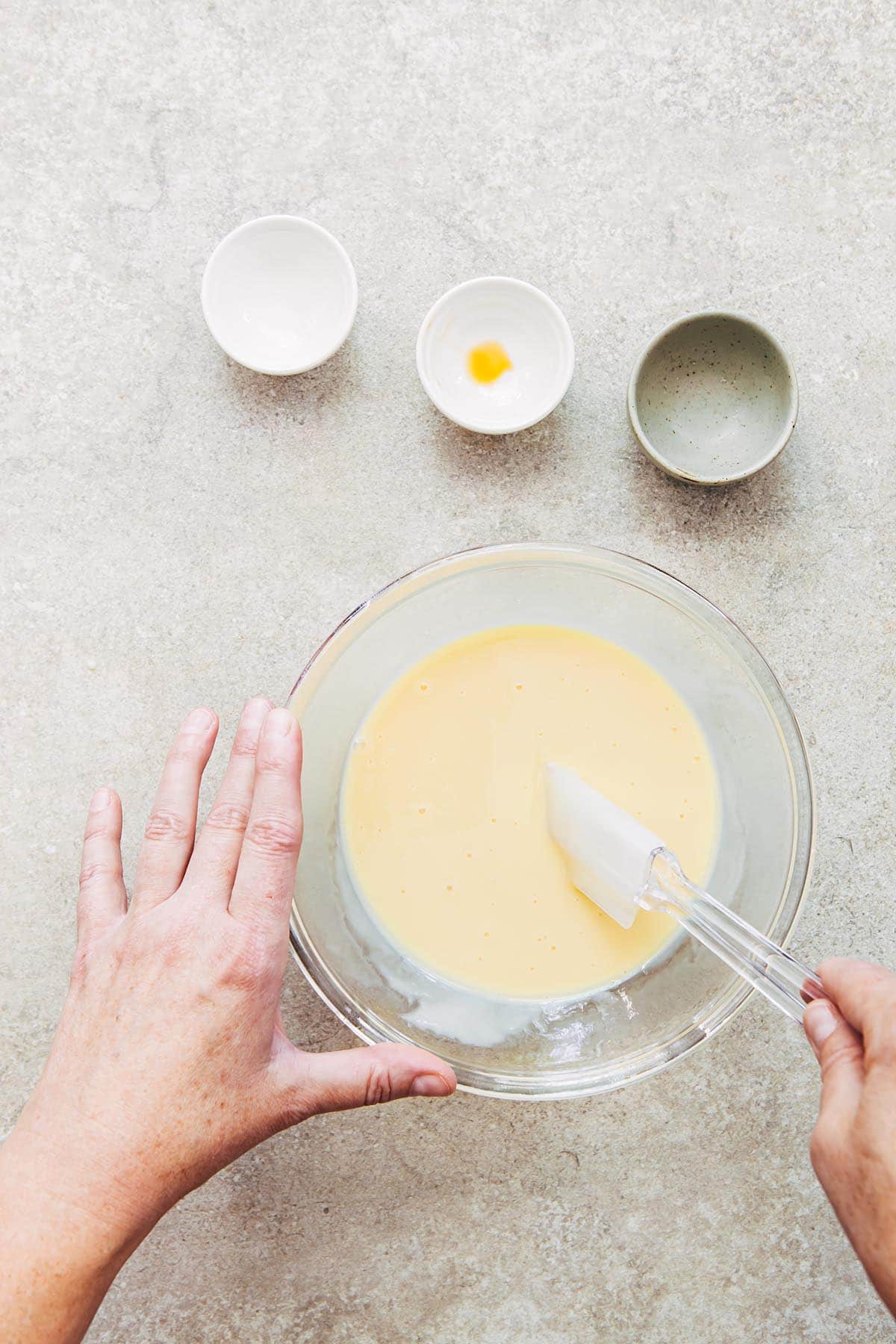 A hand stirring condensed milk in a glass bowl.