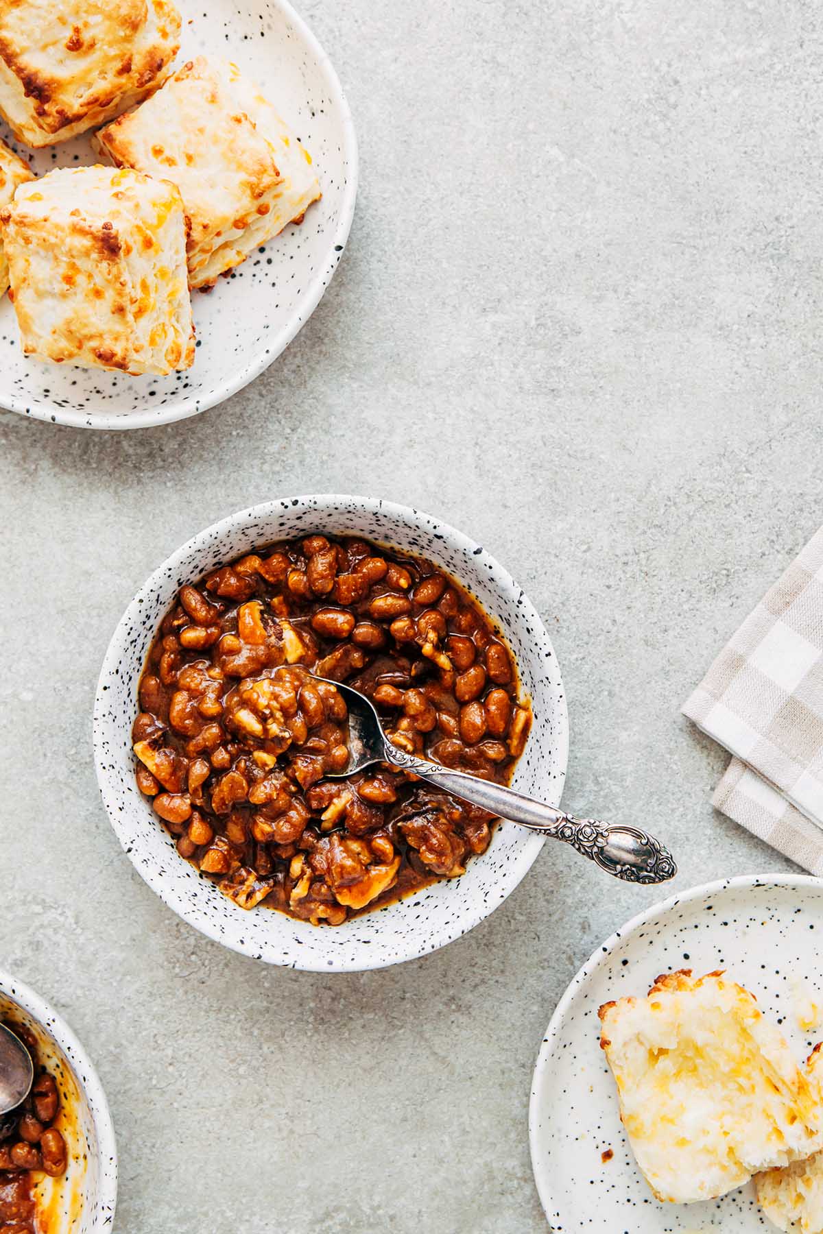 Bowls of homemade molasses baked beans and plates of cheese tea biscuits on the side.