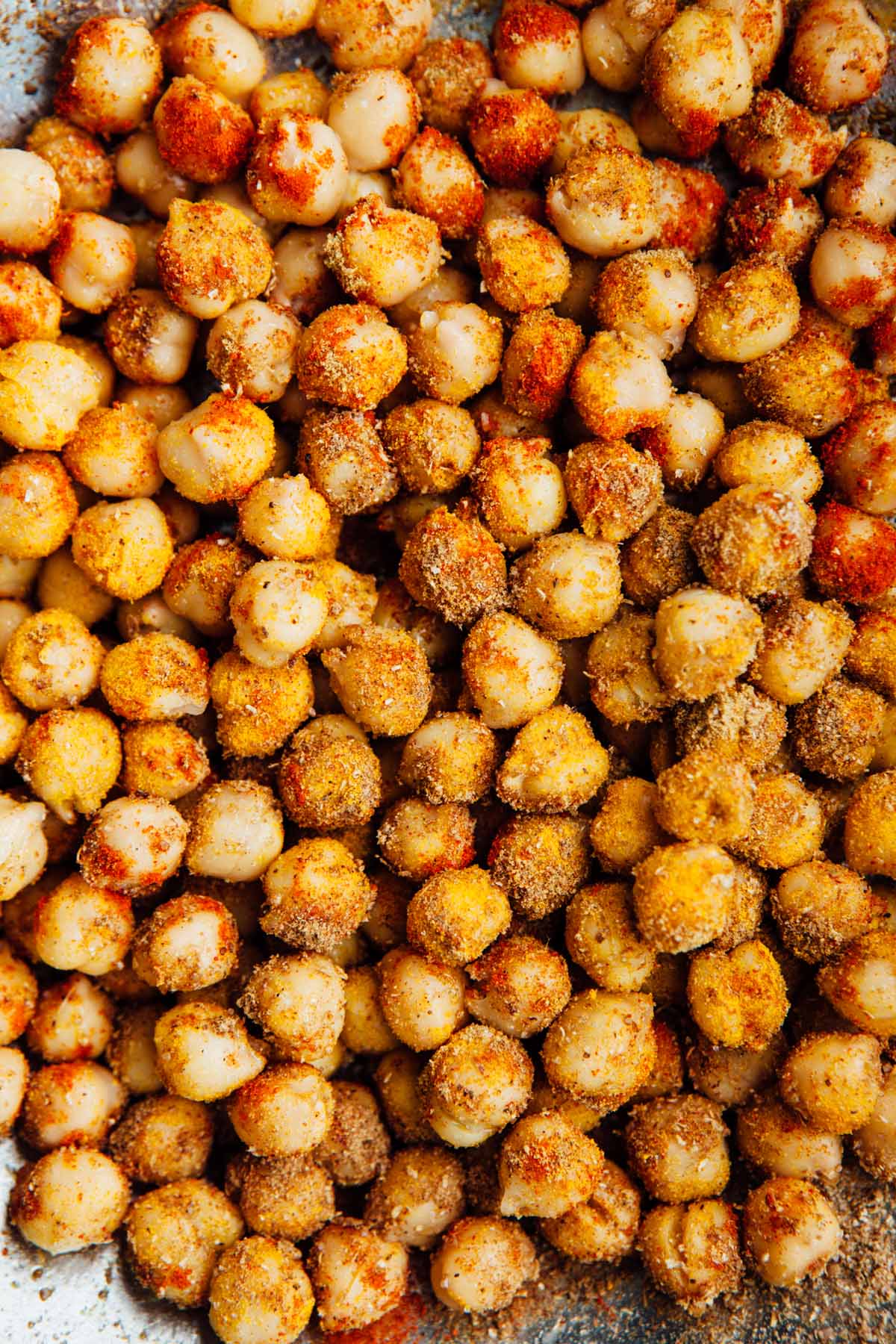 Rinsed and dried chickpeas, partially tossed with oil and spices, ready to be roasted in the oven for chickpea tacos.