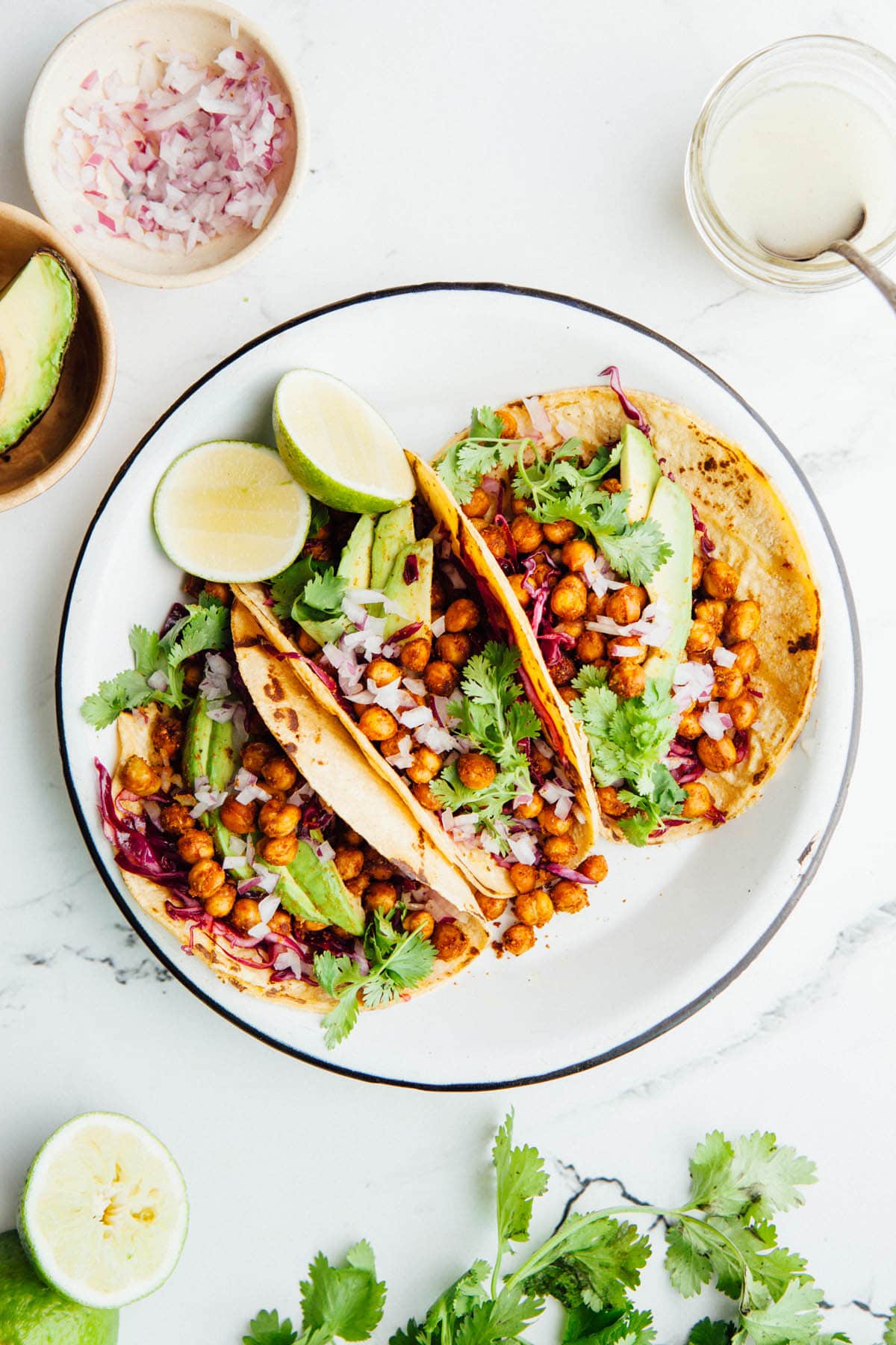 Three roasted chickpea tacos standing upright in a white round enamel plate shot from overhead.