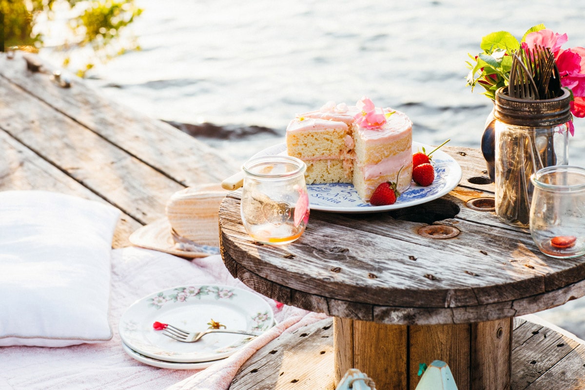 Lemon buttermilk cake with strawberry jam-cream cheese icing on a small table on a dock.