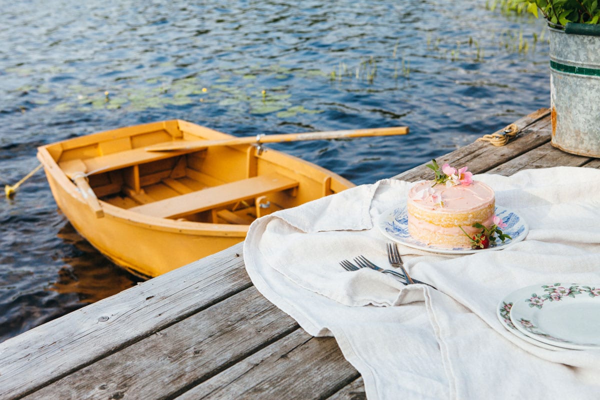 A lemon buttermilk cake on a plate on a dock next to a yellow rowboat.