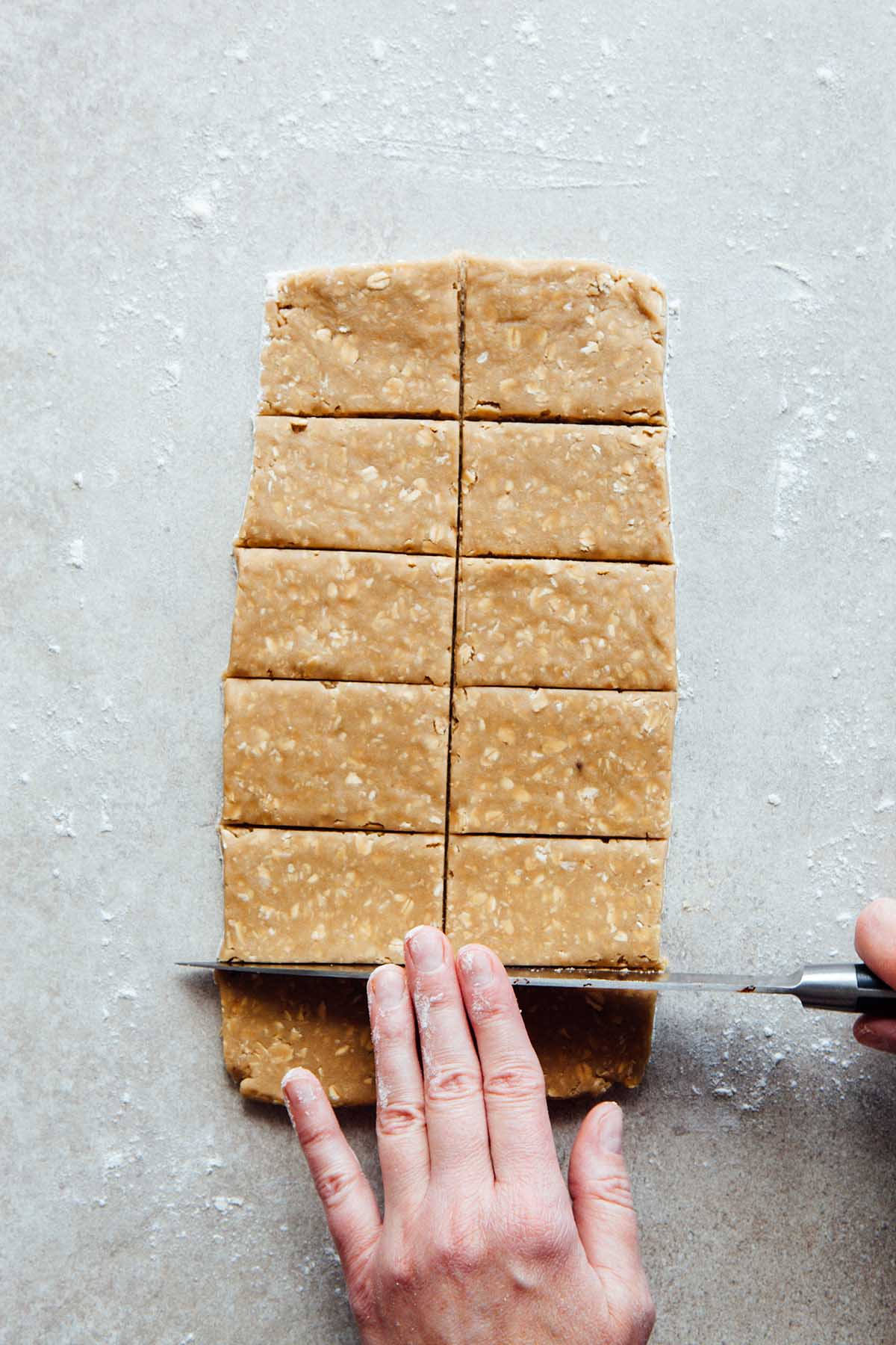 A hand slicing oatcakes into bars with a knife.