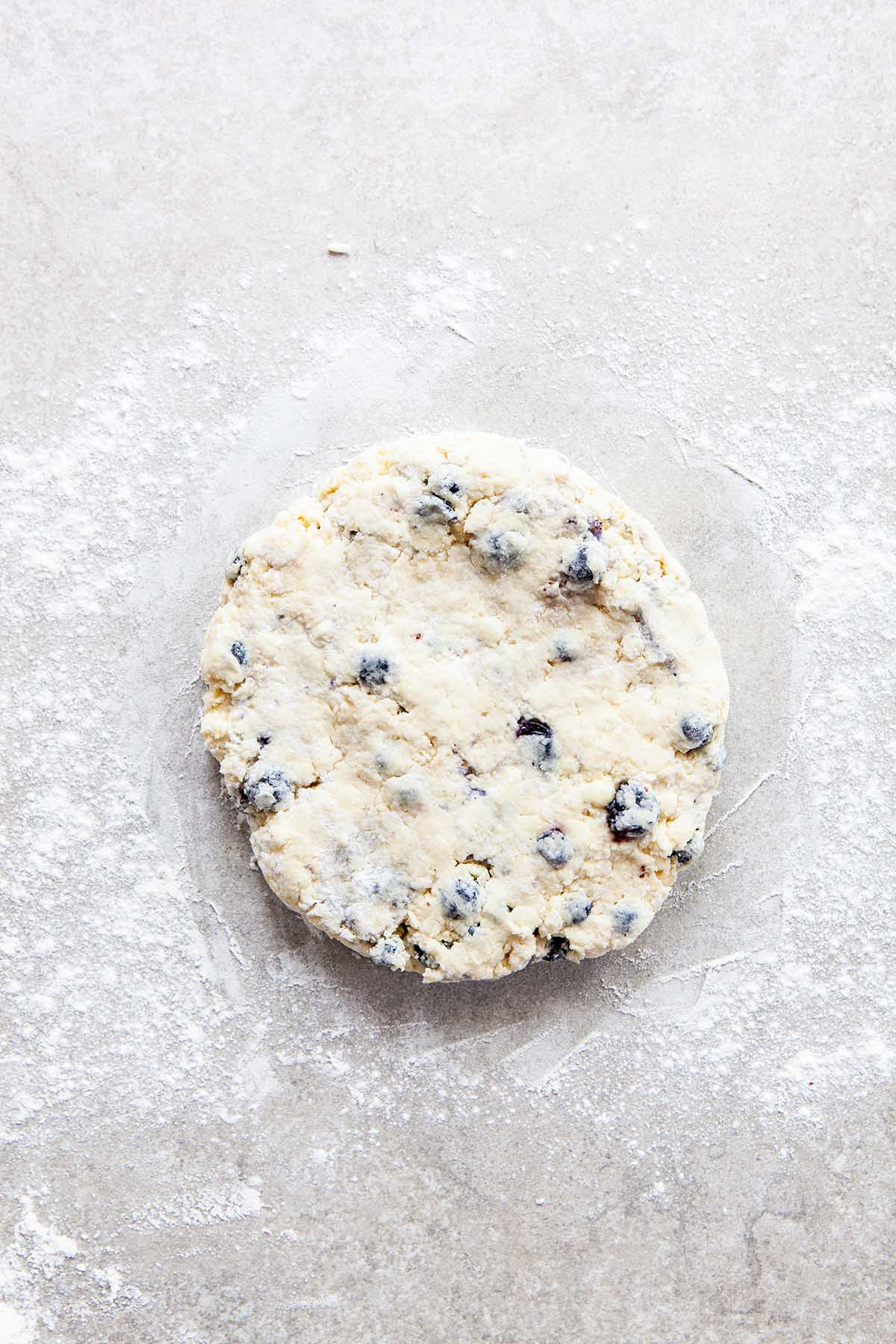 A round disc of unbaked scone dough on a floured stone surface.