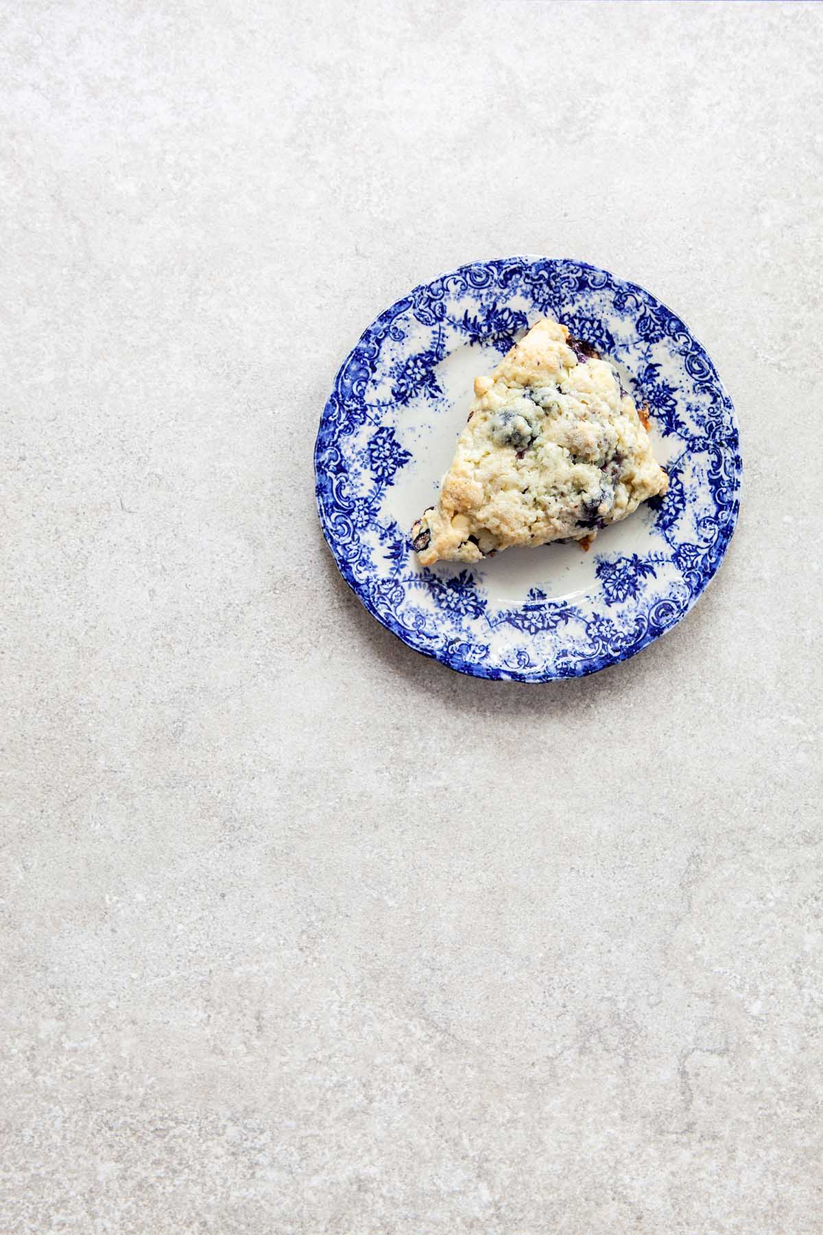 One scone on a blue and white plate on a stone surface.
