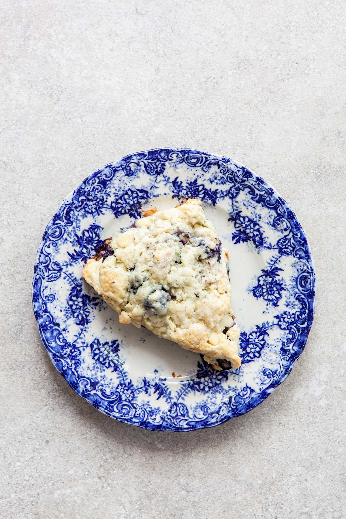 One scone on a blue and white plate laying on a stone surface.