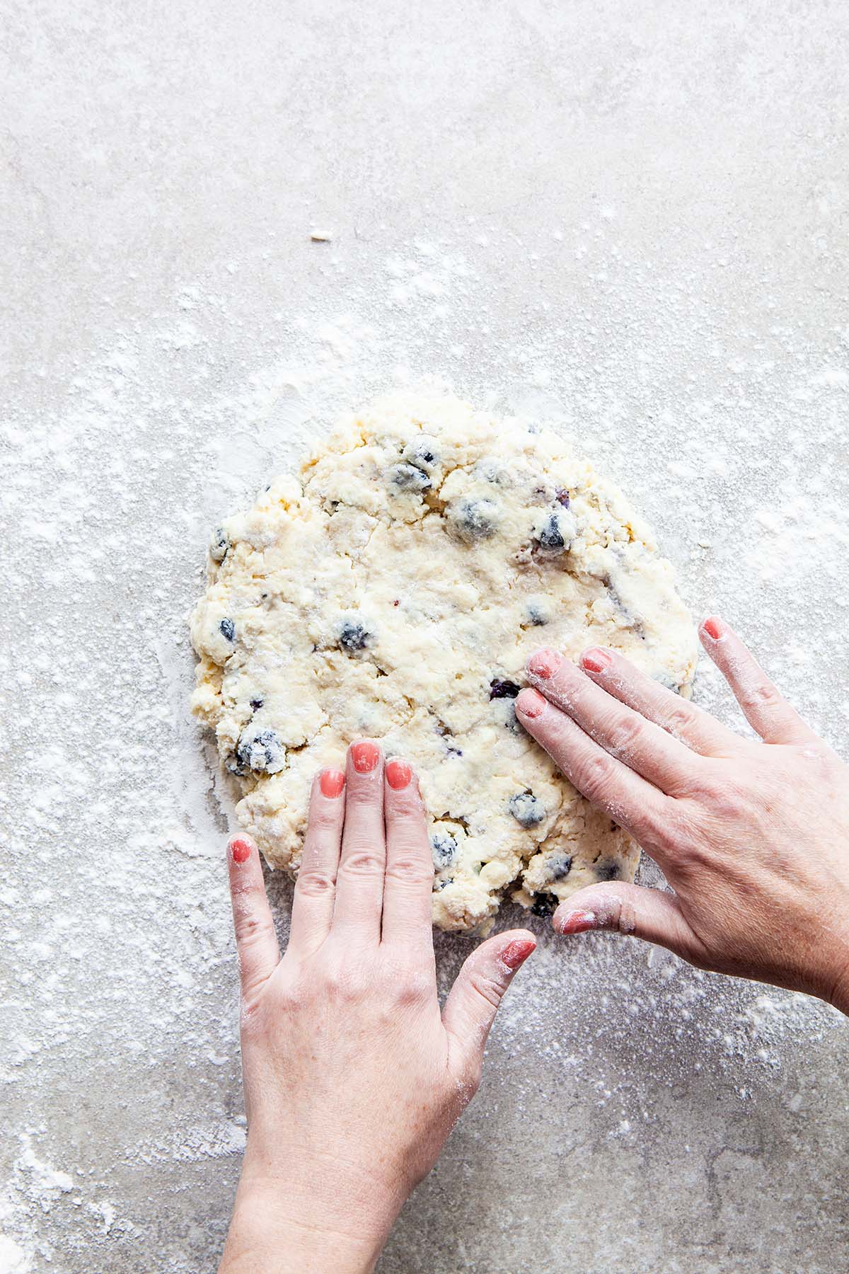 Two hands patting dough into a circle on a floured stone surface.