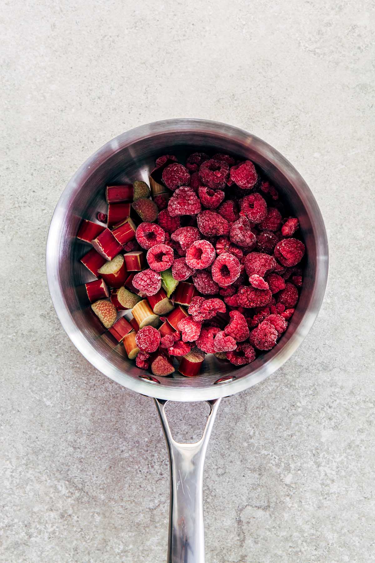 Rhubarb and frozen raspberries in a small silver pot shot from overhead.