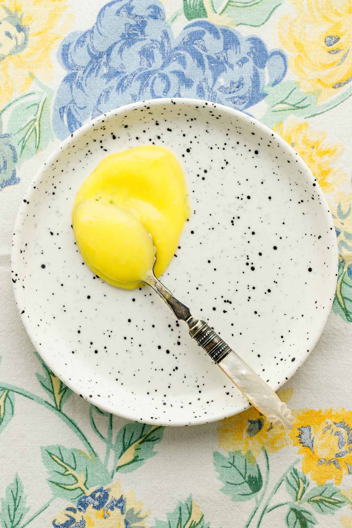 A spoonful of lemon curd laying on a small white speckled plate.