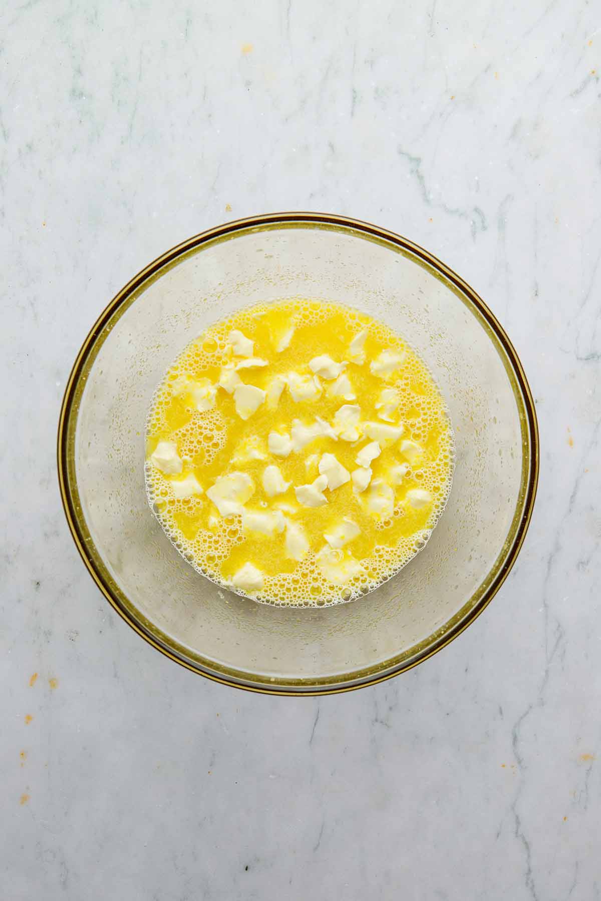 Whisked eggs, sugar, and lemon with small bit of butter floating on top in a large glass bowl.