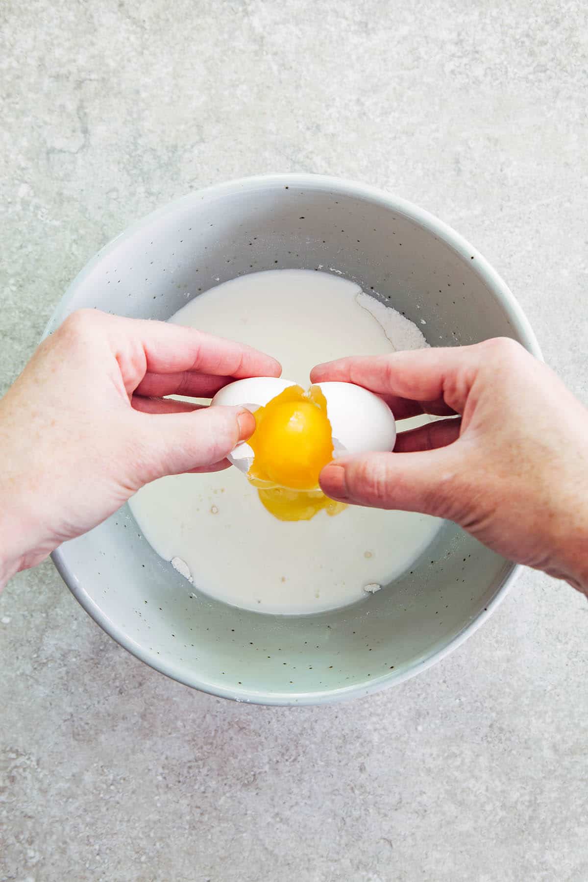 Hands cracking an egg into a bowl of batter.