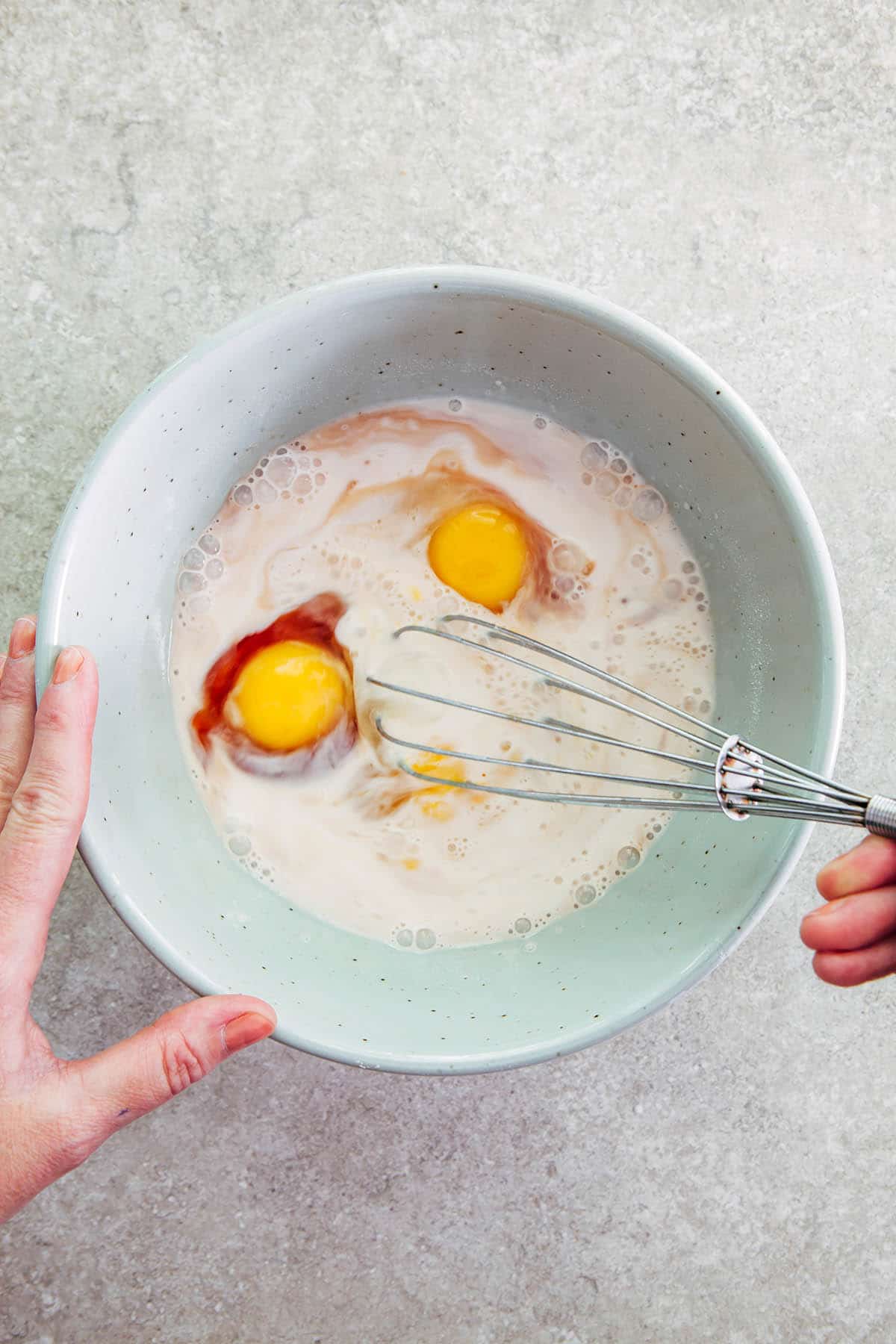 A hand using a small metal whisk to mix egg into batter.