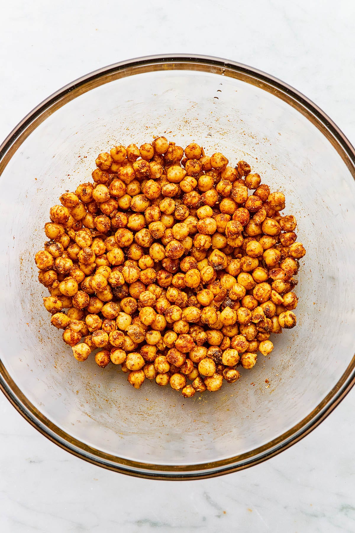 A bowl of drained rinsed chickpeas tossed with spices, salt, and oil in a glass bowl.