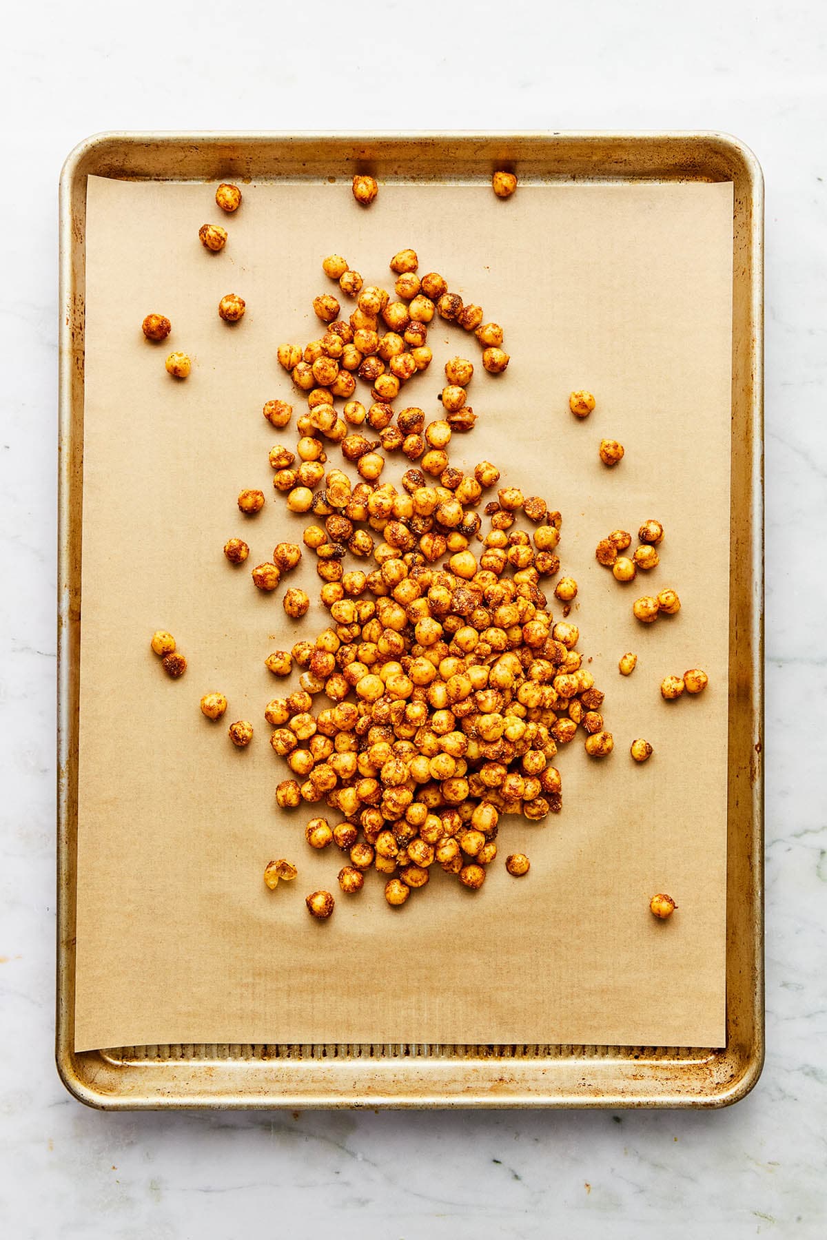 A small pile of spiced uncooked chickpeas on a baking sheet with parchment paper.